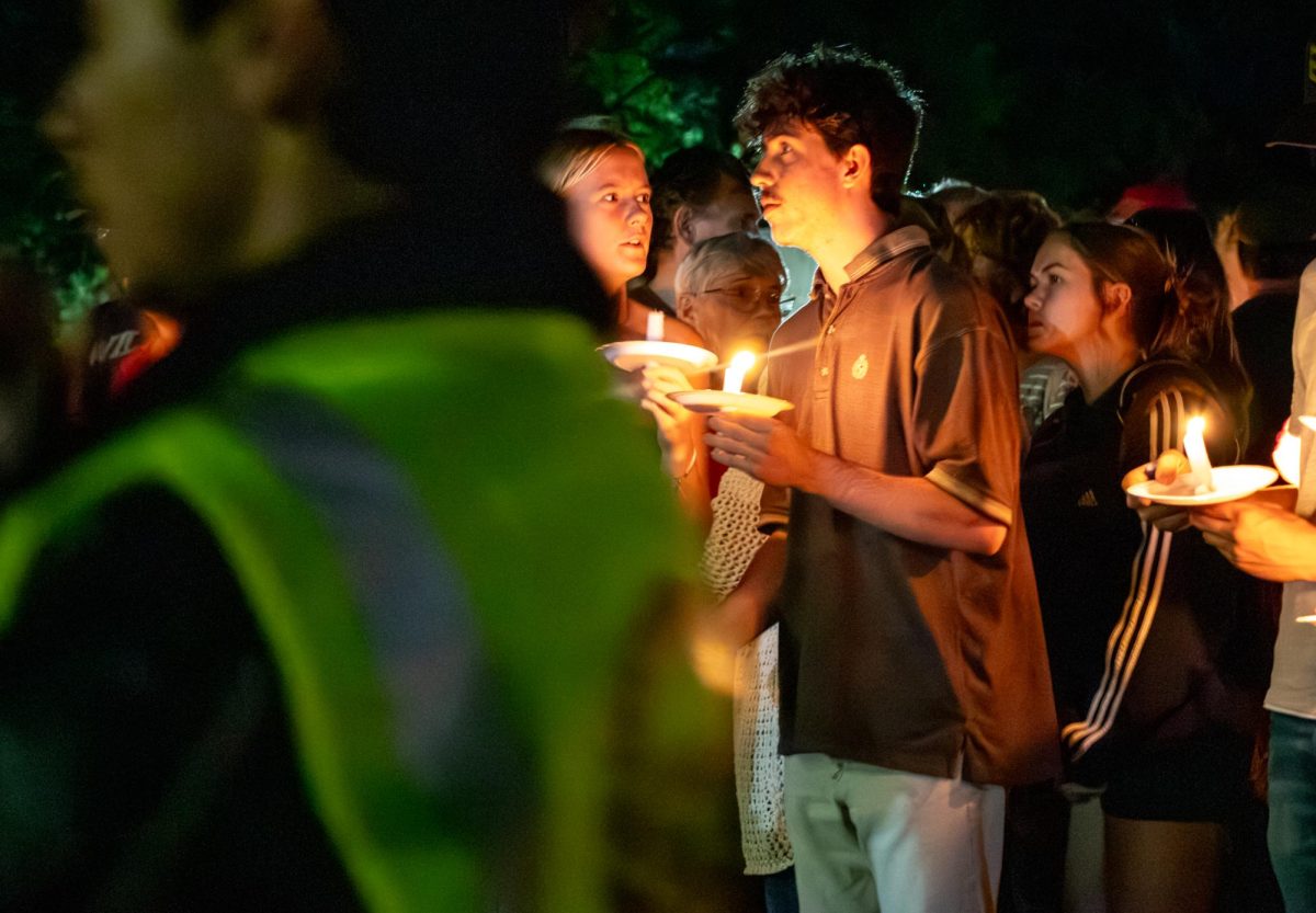 Two students hold candles and whisper amongst a sea of mourners while a student security employee monitors the gathering on the evening of 09/11. CMU's chapter of Turning Point USA hosted a vigil to remember Charlie Kirk, a conservative political activist who was murdered the day before while speaking at Utah Valley University.