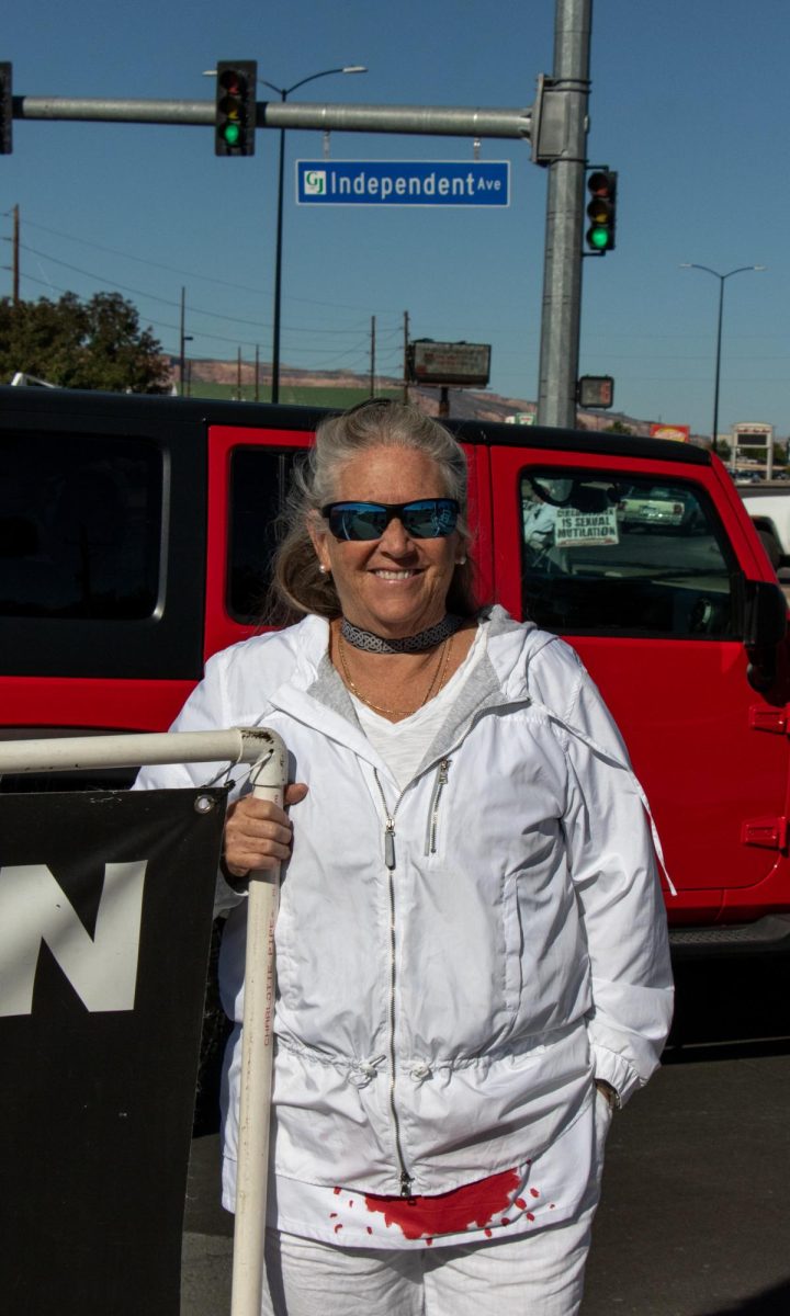 Protester Katherine Callahan smiles and holds up a sign while protesting with The Bloodstained Men. A European citizen, Callahan says that “our European doctors don’t stand by the American standard.”
